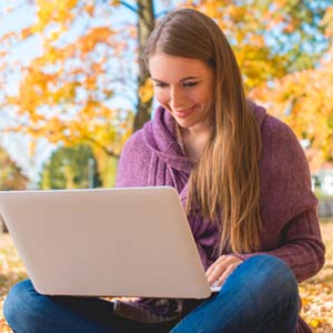 Smiling young woman sitting in leaves and working on a laptop.
