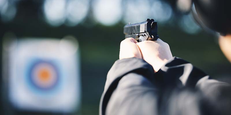 Person pointing a handgun at a target on an outdoor shooting range,